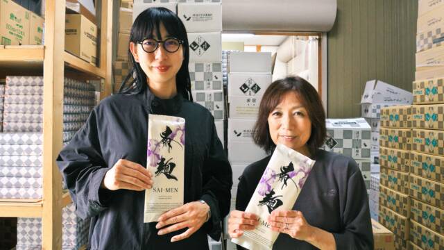 製麺所の製品の前で、「斎麺」を持つ南野マキさんと渡邉美千代さん。