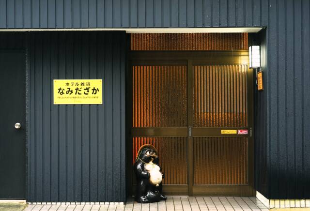 黒い壁、すりガラスの引き戸、店名が書かれた黄色い看板。信楽焼のたぬき。