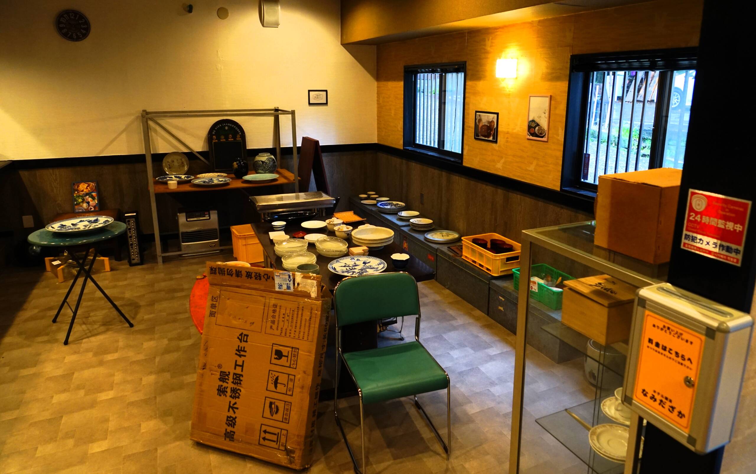 オレンジ色の照明の店内、中央に様々な大皿小皿が積まれたテーブル、奥にも模様入りの大皿が並んだ棚などがある。