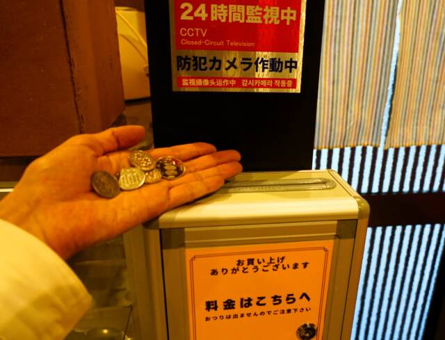 左手の手のひらに、小銭で900円を持っている。柱に備え付けられた料金箱がある。