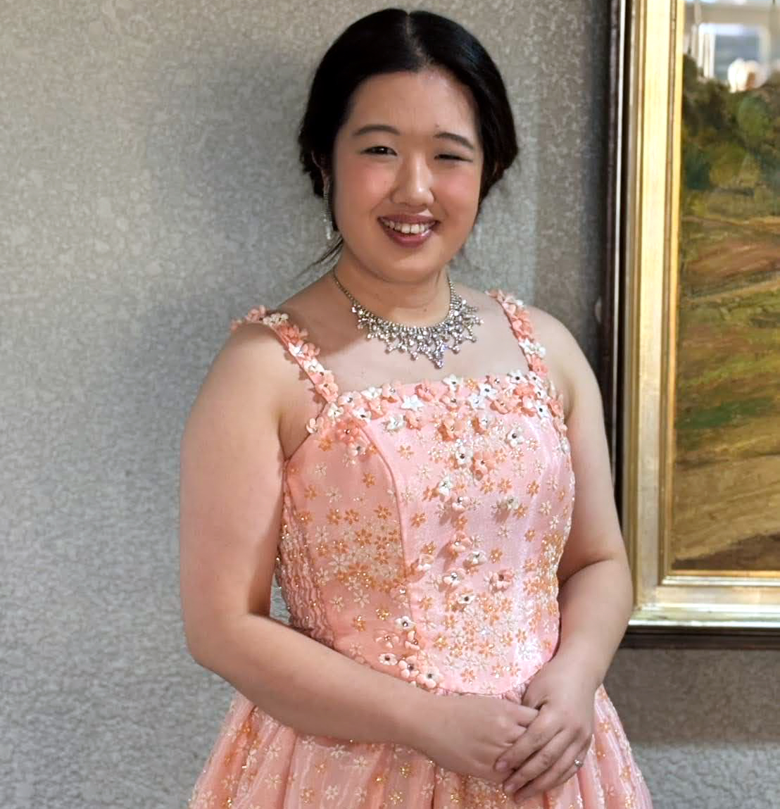 ピンク色のドレスを着て微笑む声楽家の若い女性