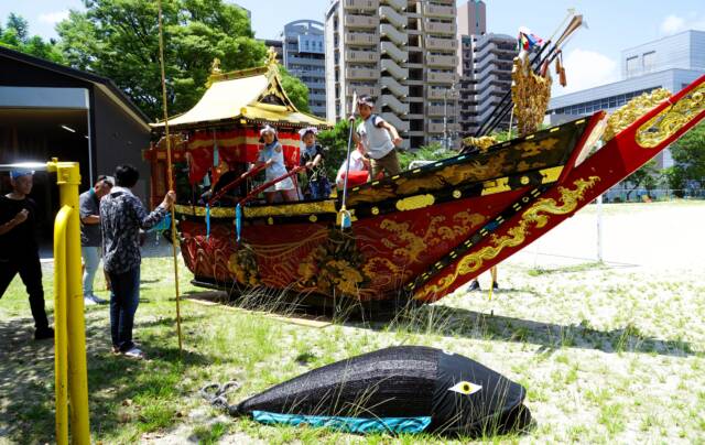鯨船勢州組の勇壮な船上で、矢を構える踊り子と櫓の漕ぎ手の子どもたち。手前の地面に張り子の鯨がある。