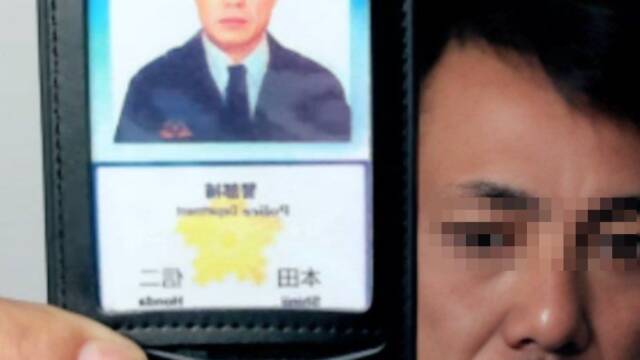 スーツにネクタイ姿の男が顔写真入りの「警察手帳」のようなものを見せている様子のスマホでのビデオ通話中のスクリーンショット。画面左上のワイプ（小窓）には電話の受け手の姿も映っている。