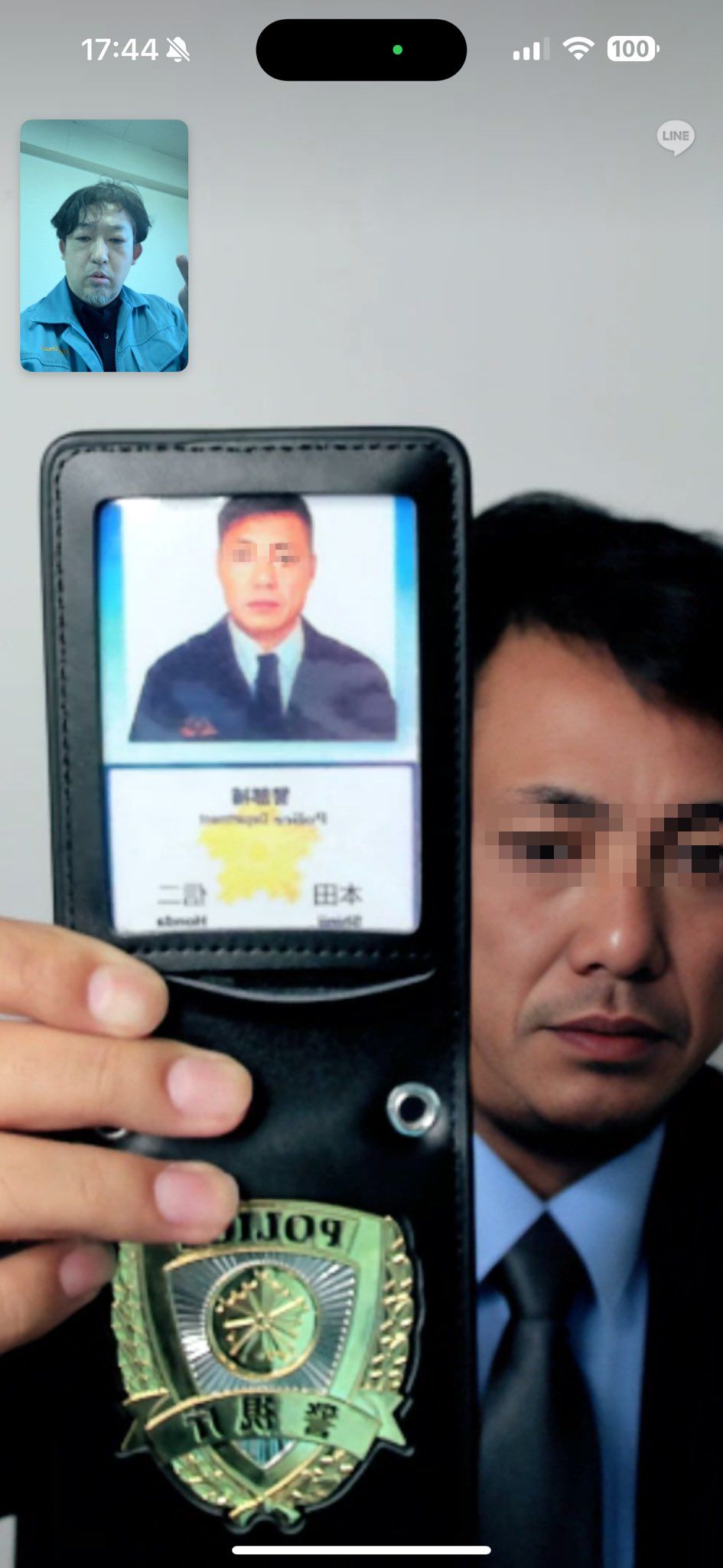 スーツにネクタイ姿の男が顔写真入りの「警察手帳」のようなものを見せている様子のスマホでのビデオ通話中のスクリーンショット。画面左上のワイプ（小窓）には電話の受け手の姿も映っている。
