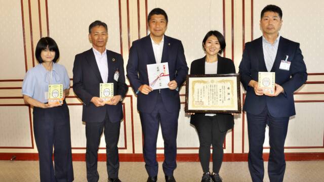 5人の人が並んで立っている。右から書籍を持った関係者、感謝状を持った精神科医さわさん、目録を持った森市長、書籍を持った関係者2人。