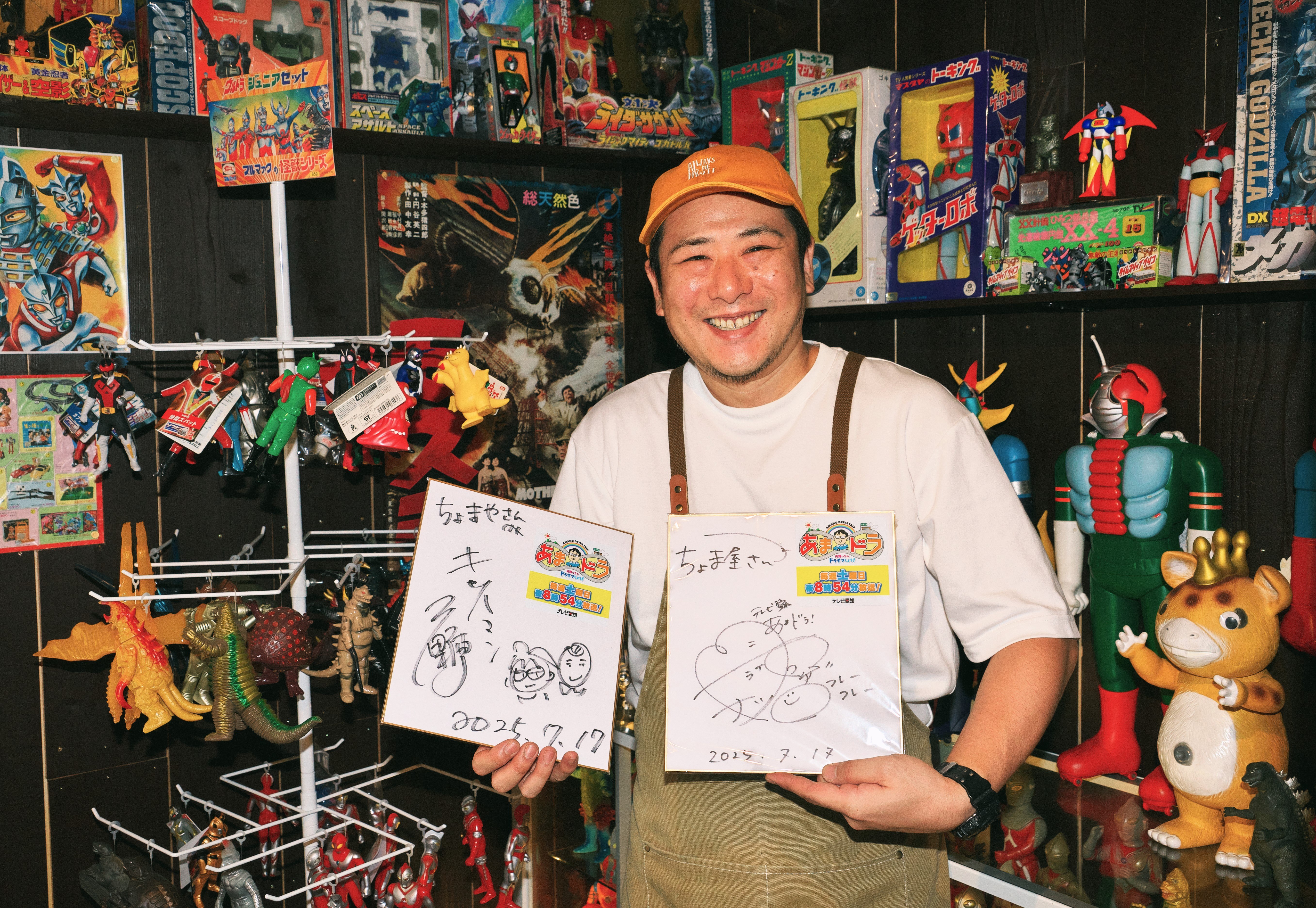 所狭しと並べられた昭和のおもちゃコレクションを前に、サイン色紙を両手に持ち笑顔の店主の姿