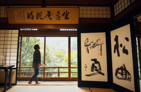 寿亭水雲閣の和室に展示された書と大きなガラス窓から御在所の風景が見える様子