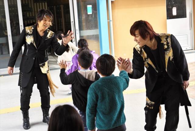 KUNI-KENがライブ終了後、体育館出口で児童とハイタッチを交わしながら見送る場面。