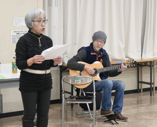 立って朗読をする出口さんとその後ろでギターを弾く竹内さん