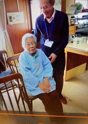 椅子に座る高齢の女性と後に立って見守る男性