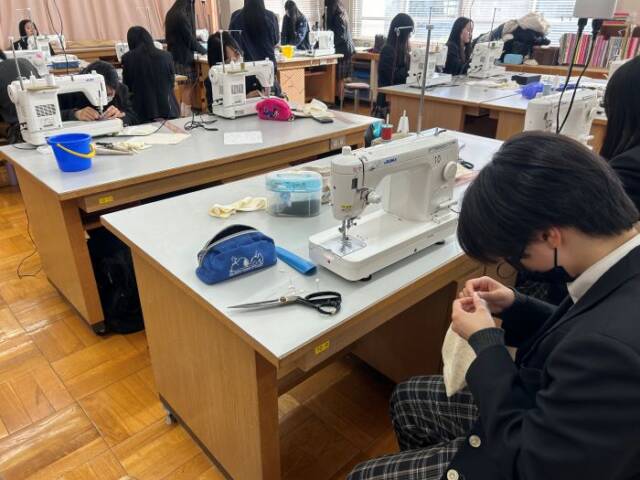 被服室で布団を作る服飾経営コースの生徒。ミシンや裁縫道具が並ぶ
