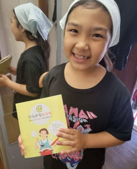 ひらがなレシピと書かれた冊子を手に笑顔を見せる子ども