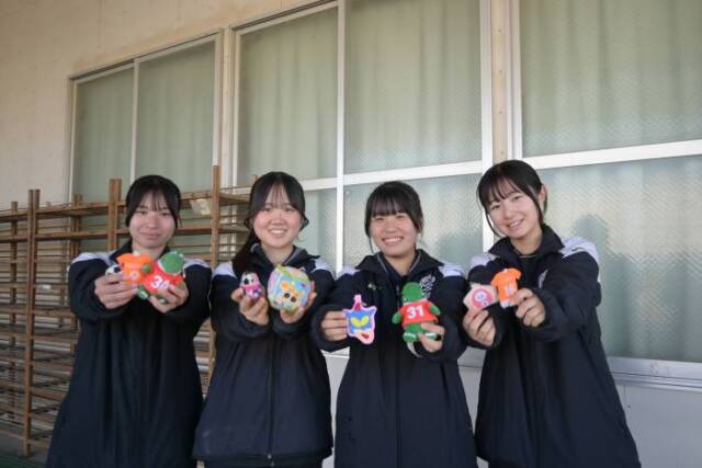 手作りのお守りを2つずつ持って微笑む部員とマネージャー
