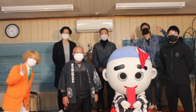 四日市市のこにゅうどうくんが、舌を引っ張りながら前列に立ち、その横に安藤選手や高木煙火の関係者が立つ。後列にゲストが立つ