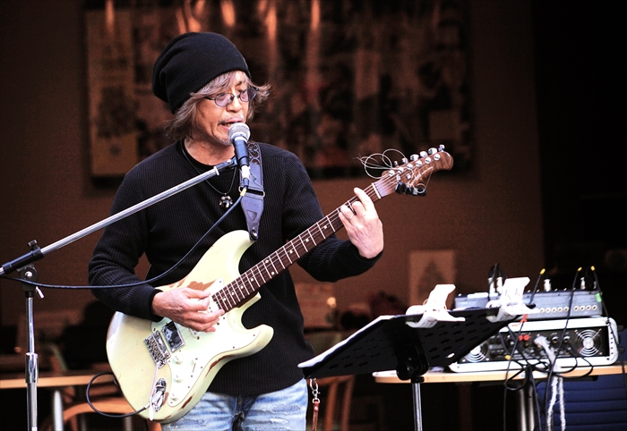 屋外ステージで歌うロッシーさん。100回記念イベントのトリを務めている様子