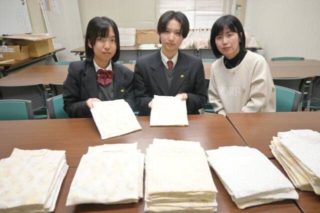 棺に入れる赤ちゃんの布団を置いて、手にも布団を持つ四日市農芸高校の生徒と、中村教諭（右）