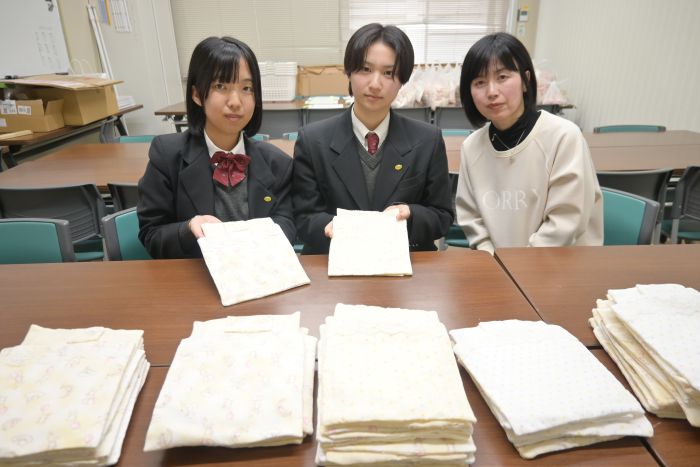 棺に入れる赤ちゃんの布団を置いて、手にも布団を持つ四日市農芸高校の生徒と、中村教諭(右)