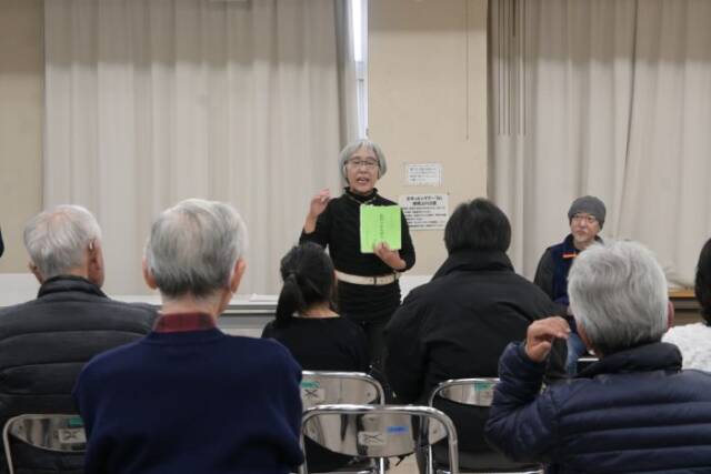 旧四日市を語るの冊子を手に語る出口さんとその話を聞く参加者。出口さんの話を聞く竹内さんが後にいる