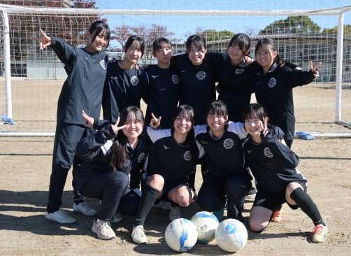 サッカーゴールの前で2列で肩を組む四日市南高校女子サッカー部員