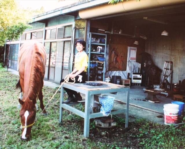 工房前でコークス炉に腰掛ける銅谷さん。傍らには馬がいる。