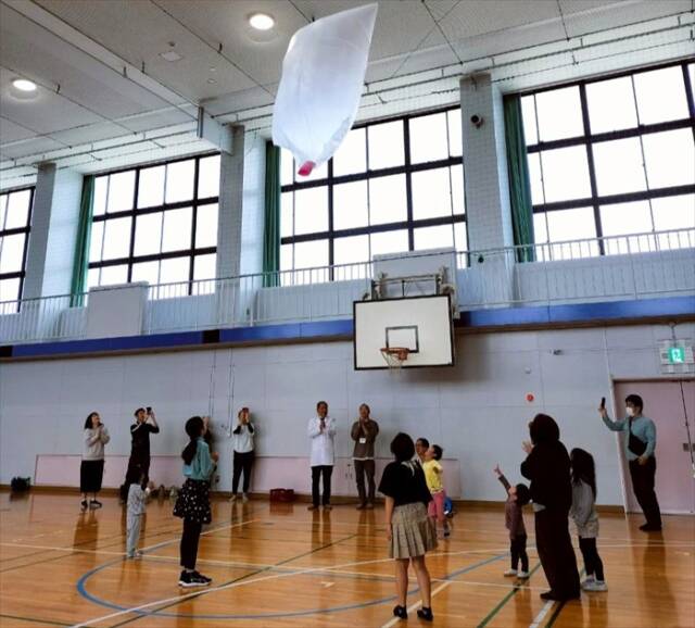 プレイベント「熱気球をあげよう」で、参加者らが宙に浮かぶ熱気球を見上げる様子