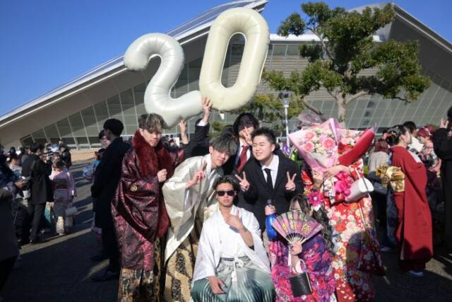2と０の形のバルーンを手にして記念写真を撮る振袖や羽織袴の男女
