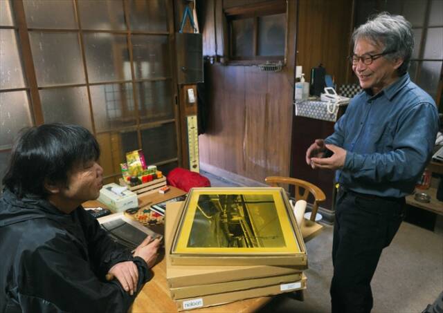 写真家・松原豊さんが、農家の松本一夫さんにお茶で染めた写真作品の制作過程を説明する様子