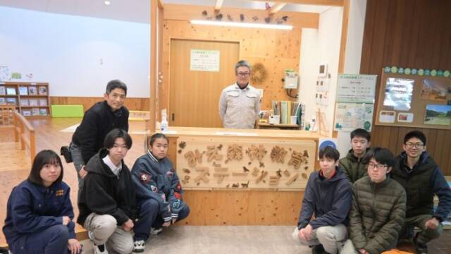 みえ森林教育ステーションの看板を囲む部員と教員とステーション担当者