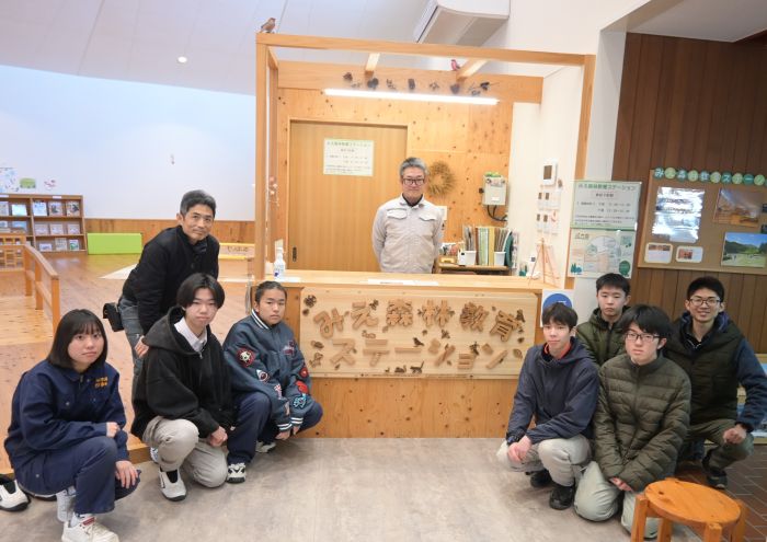 みえ森林教育ステーションの看板を囲む部員と教員とステーション担当者