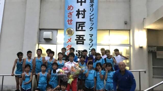 東京五輪出場を祝した懸垂幕の前で花束を持ち後輩の小学生と記念写真を撮る中村選手