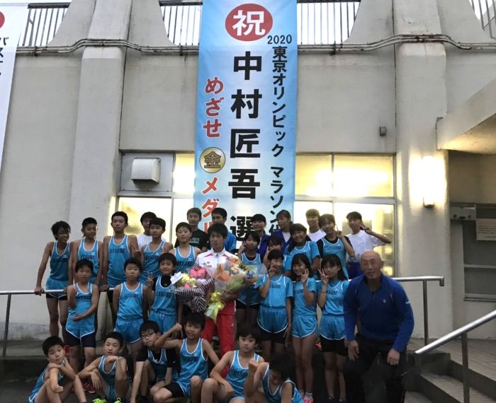 東京五輪出場を祝した懸垂幕の前で花束を持ち後輩の小学生と記念写真を撮る中村選手