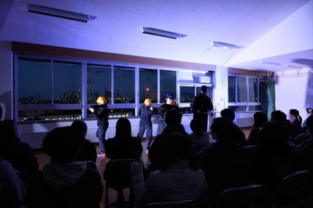 3階練習室での「プリオシン海岸」のシーン。窓の外に広がる四日市の夜景が、銀河鉄道の車窓のように観客の目に映る。