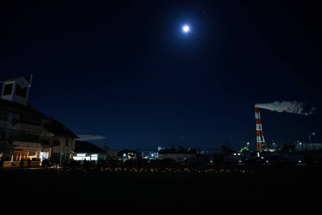 三浜文化会館の校庭に置かれた折り紙リンゴの灯りが天の川を描き、遠くに工場夜景が見える。