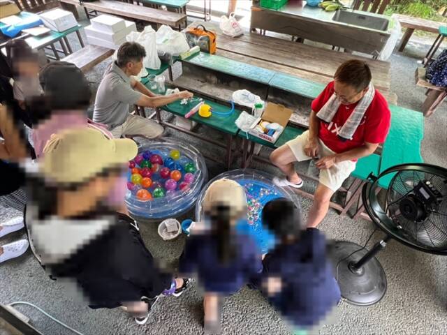 夏祭り風に用意された水風船釣りで遊ぶ子どもたちとロータリークラブ会員の様子