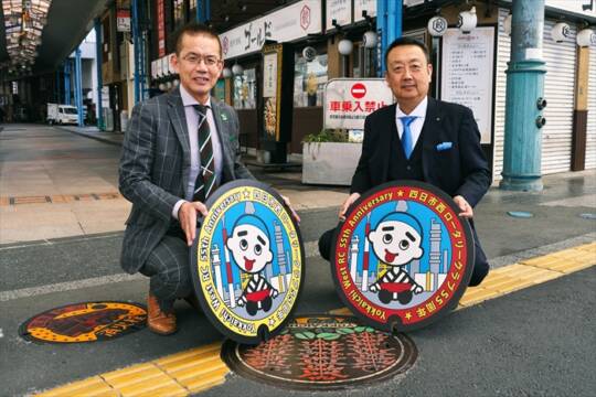 諏訪栄町の歩道でデザインマンホールのレプリカを持つ佐野貴信会長と田中大補実行委員長