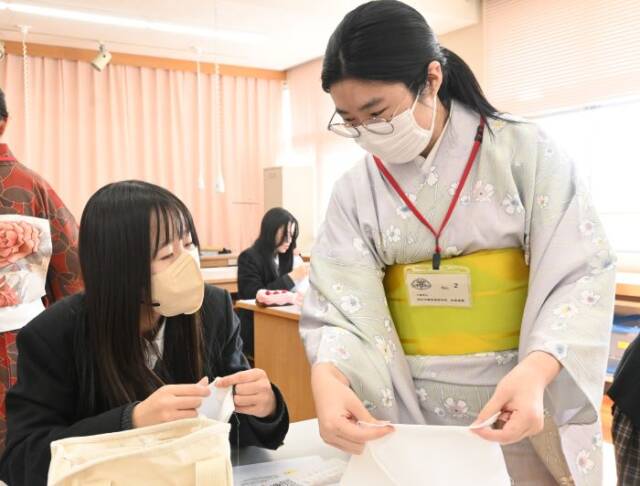 着物を着た諸岡さんが生徒に縫い方を教える姿