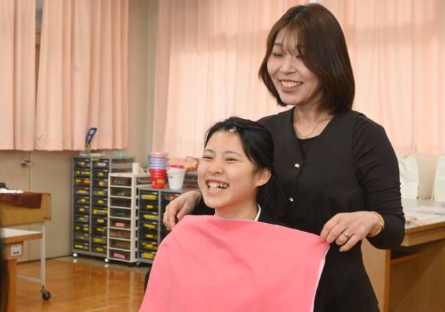 パーソナルカラー診断のためにコーラルピンクの布を生徒の顔に合わせる