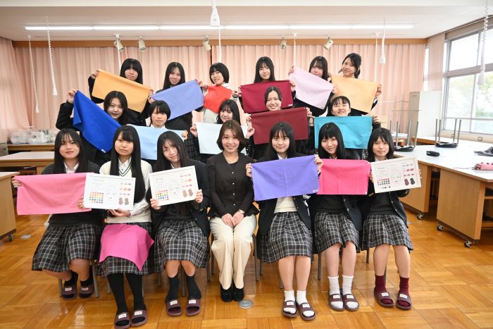 パーソナルカラー診断に使う色見本の布を手にし、清水さんと記念写真を撮る生徒