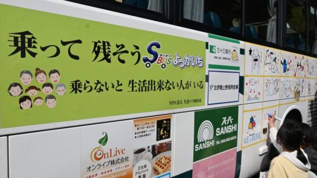 乗って残そうせいかつばBUSよっかいちと書かれたステッカーの横に絵を描く子ども