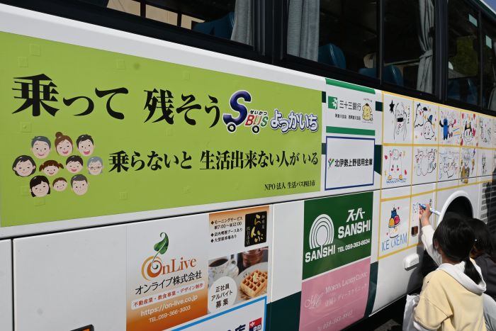 乗って残そうせいかつばBUSよっかいちと書かれたステッカーの横に絵を描く子ども