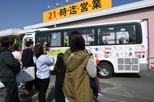 出発するバスを子どもたちや保護者が見送っている