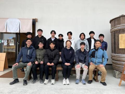 酢専門店の前で木工部の生徒が作ったベンチに座る伊藤社長と伊藤教諭と部員と副顧問の教諭