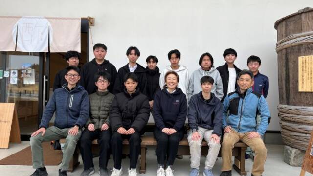 酢専門店の前で木工部の生徒が作ったベンチに座る伊藤社長と伊藤教諭と部員と副顧問の教諭