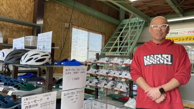 学校指定に上靴や体育館シューズを販売する店に立つ社長