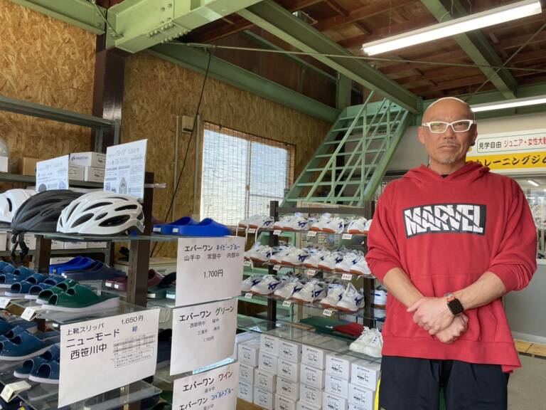 学校指定に上靴や体育館シューズを販売する店に立つ社長