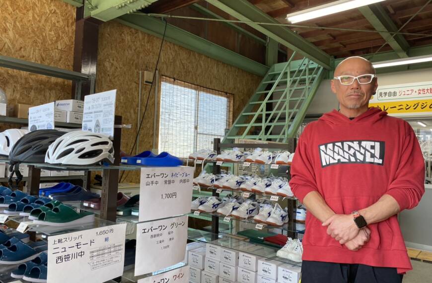学校指定に上靴や体育館シューズを販売する店に立つ社長