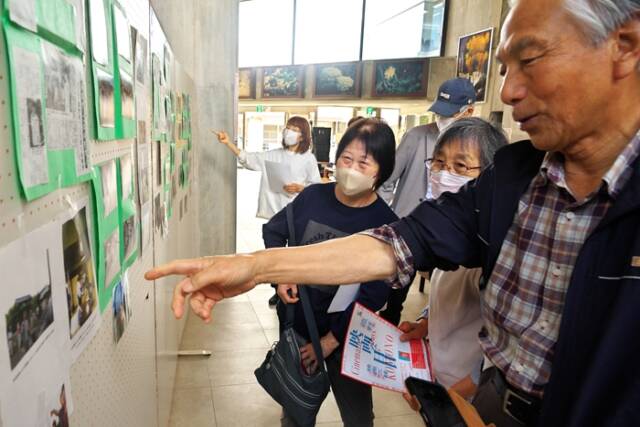 自宅が映ったロケ写真を指差して説明する来場者