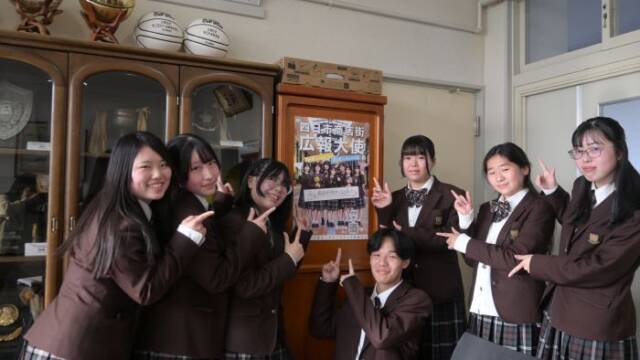 昨年のポスターを指さす今年の生徒７人