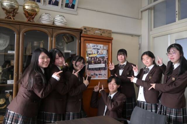 昨年のポスターを指さす今年の生徒7人