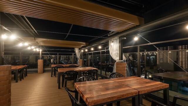プラトンホテル四日市屋上ビアガーデンの全天候型テラス席。ウッドデッキにテーブルと椅子が並び、夜景が広がる